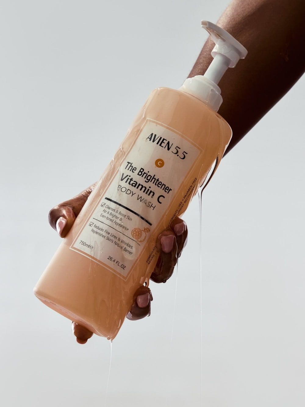 A hand grips a bottle of Avien 5.5 Vitamin C body wash as it pours over the fingers.