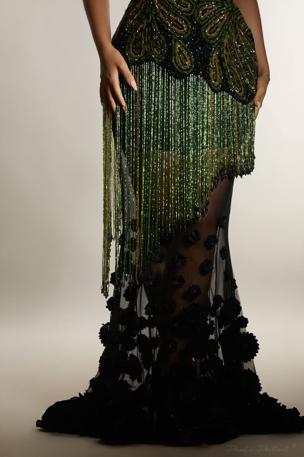 Close on a gown: strands of green beading fall over a sheer black skirt.