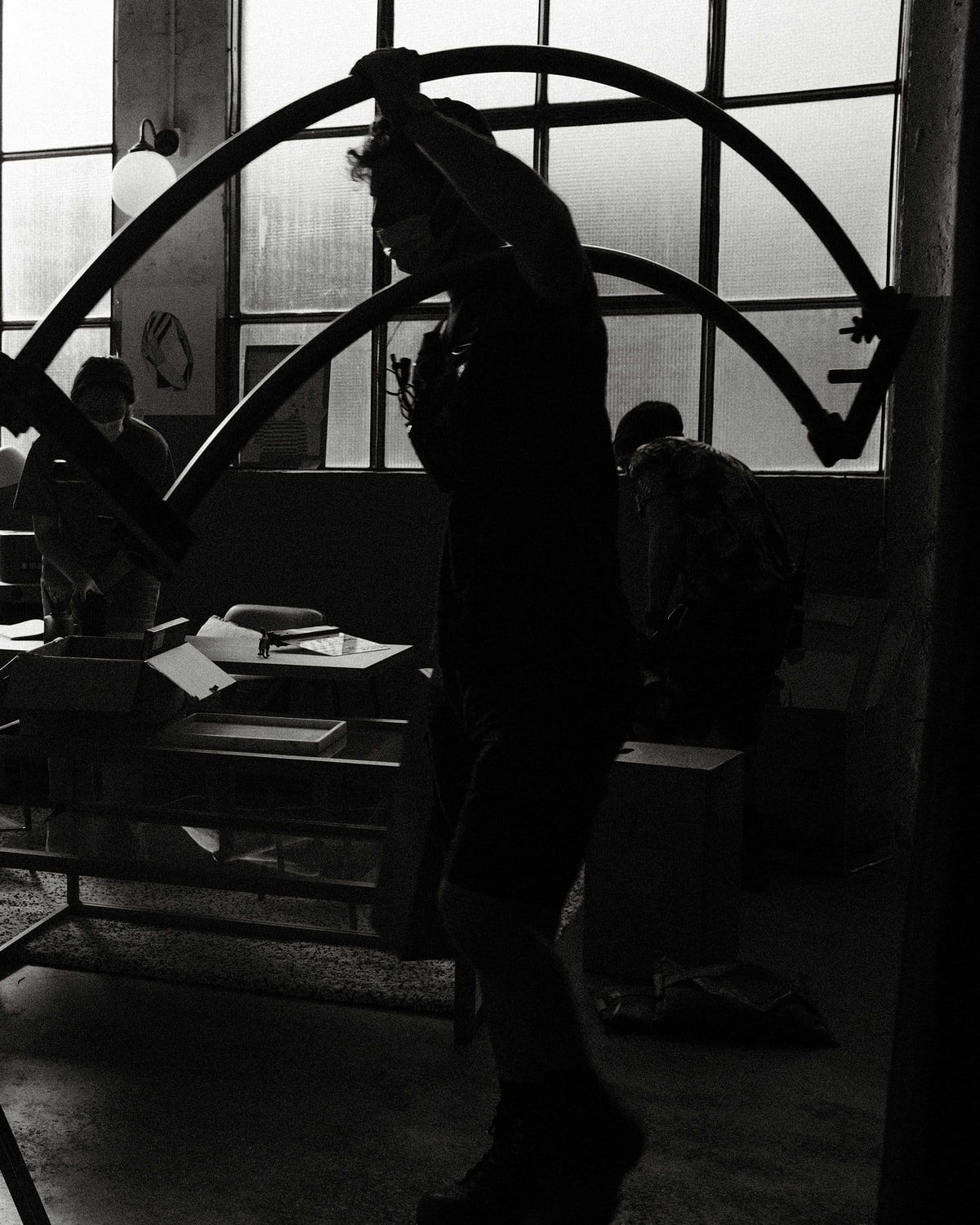 Silhouetted in a studio, a crew member lifts a curved frame into place while others work on the set behind.