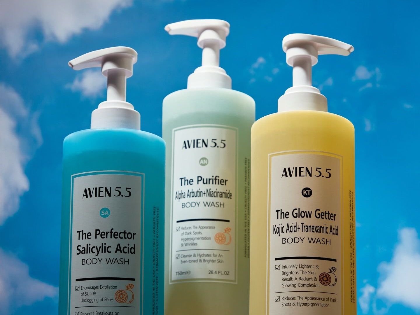Three Avien 5.5 body washes, blue, green and yellow, stand on pastel blocks against a bright sky.